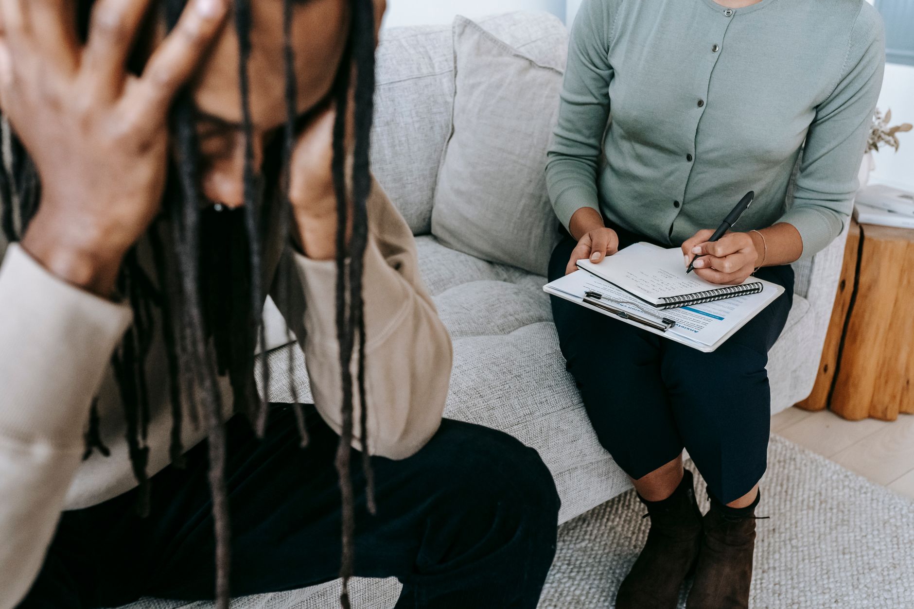 Crop concerned African American male sitting on sofa with female psychologist and holding head in hands in dismay during psychotherapy session — UPI Study