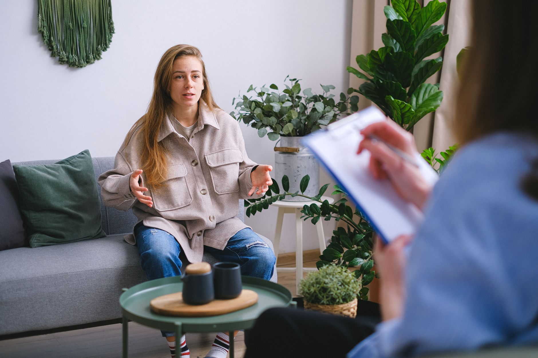 Concerned female client siting on couch and speaking about mental problems during psychotherapy appointment with blurred psychologist in light office — UPI Study
