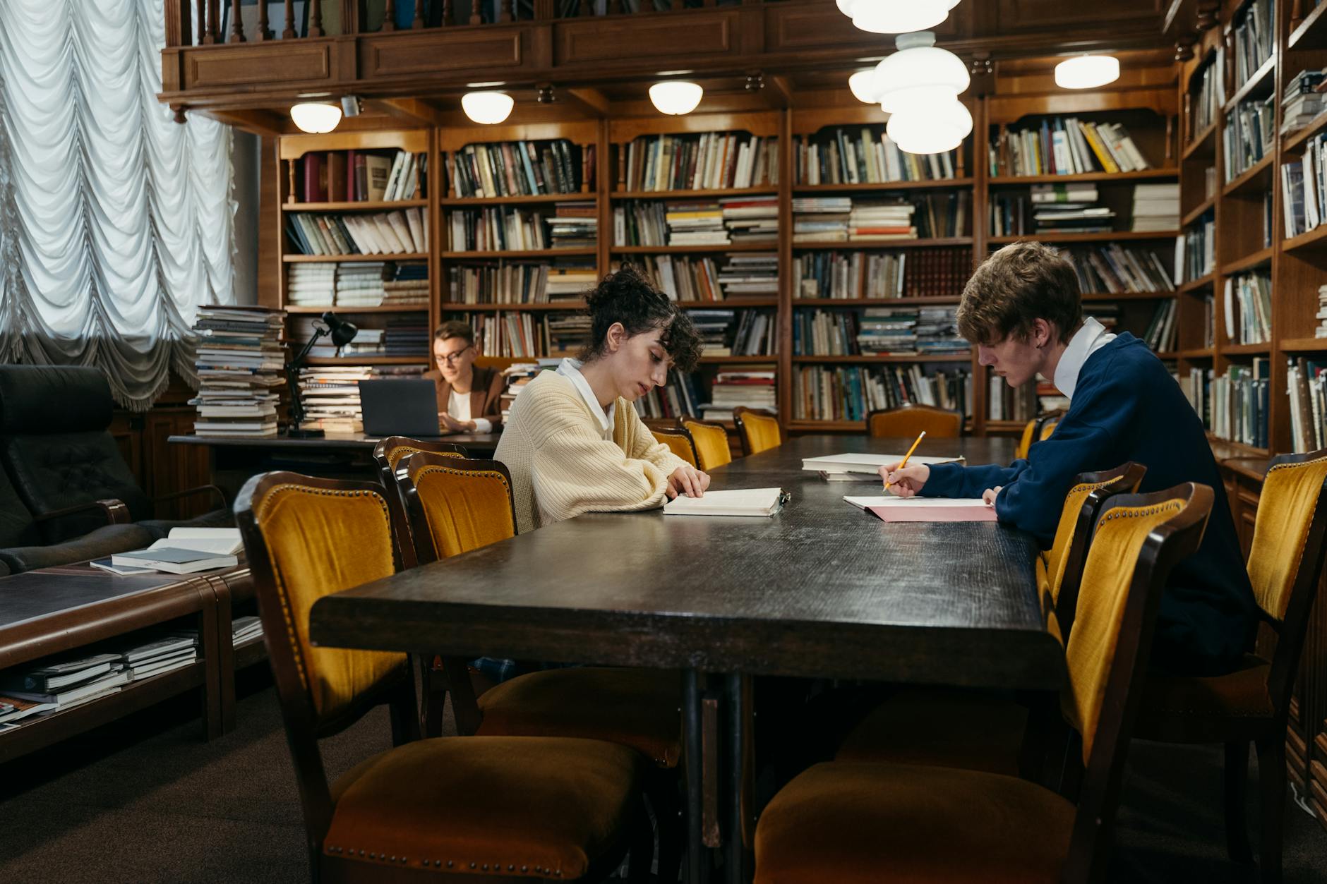 Group of students diligently studying in a traditional library filled with books, tables, and dim lighting — UPI Study