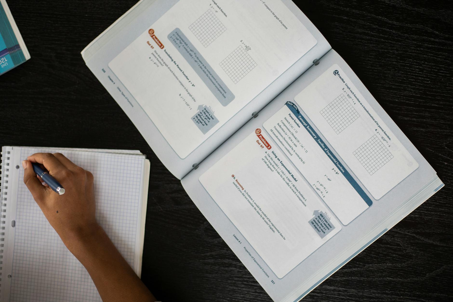 Top view of faceless African American student taking notes in notepad while sitting at table with textbook during lesson in class — UPI Study