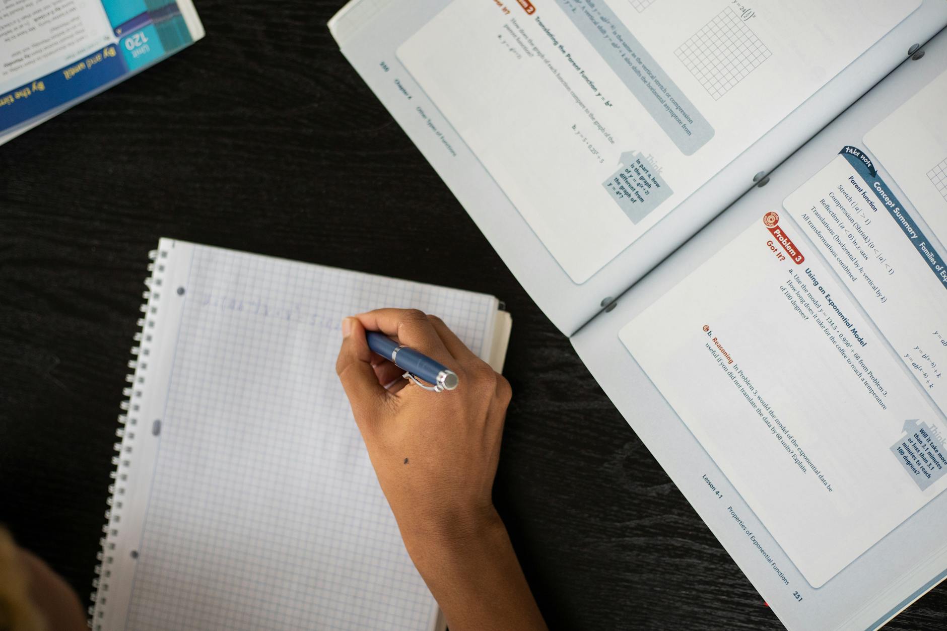 Top view of anonymous African American student taking notes in workbook at table with textbook while studying in classroom during lesson — UPI Study