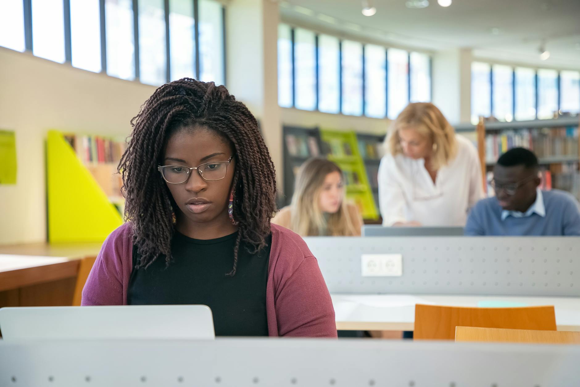 Concentrated African American female student surfing laptop while diverse classmates discussing study task with teacher — UPI Study