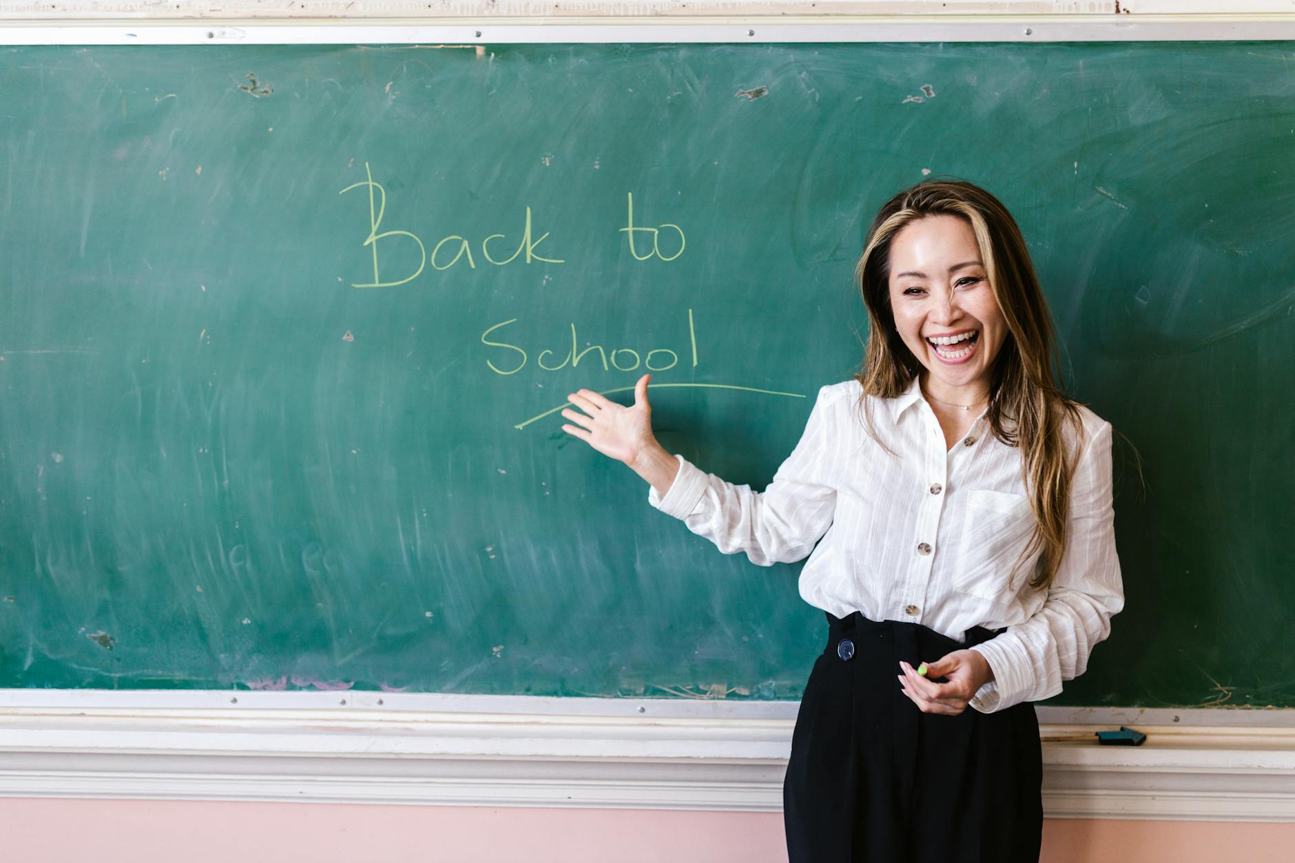Smiling teacher in a classroom pointing at back to school message on a chalkboard — UPI Study