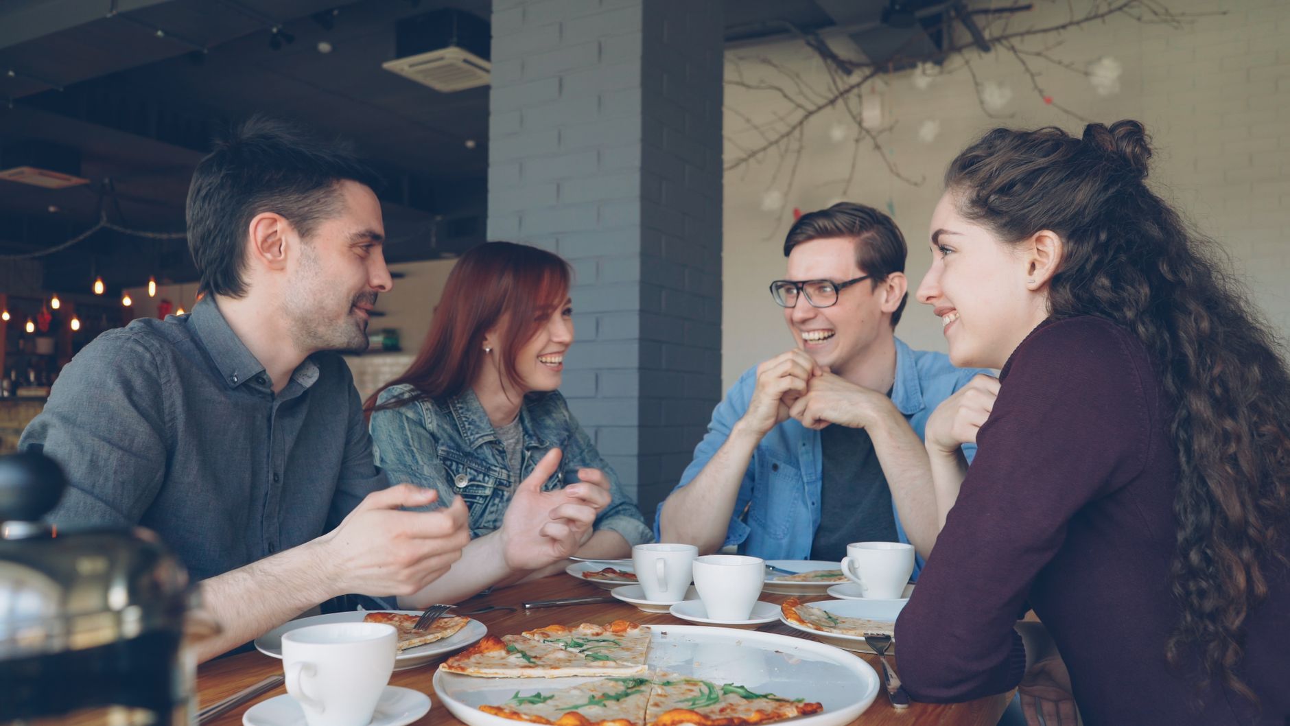 A group of friends having a fun conversation over pizza and coffee in a modern cafe, enjoying leisure time together — UPI Study