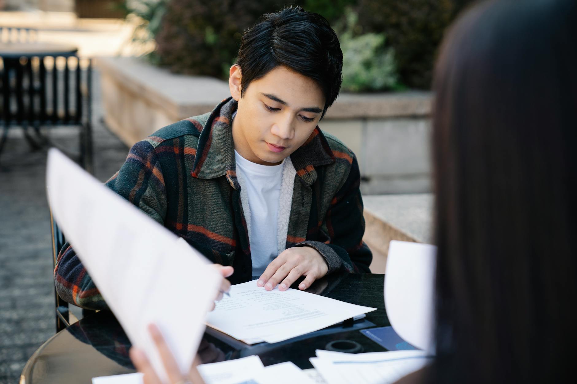A focused young Asian man studying at an outdoor table, preparing for exams — UPI Study