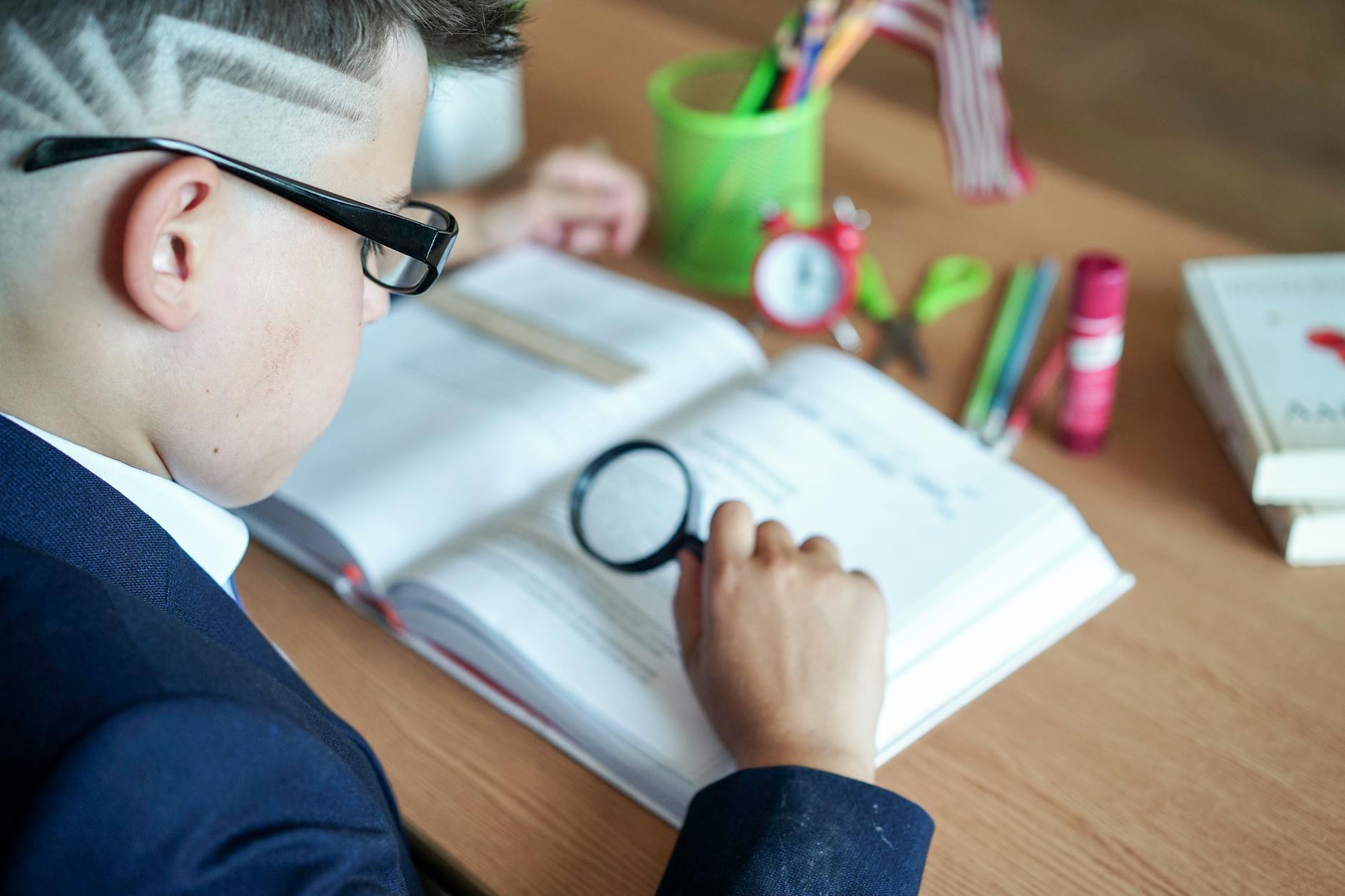 A young boy focuses on his book using a magnifying glass at a study desk — UPI Study