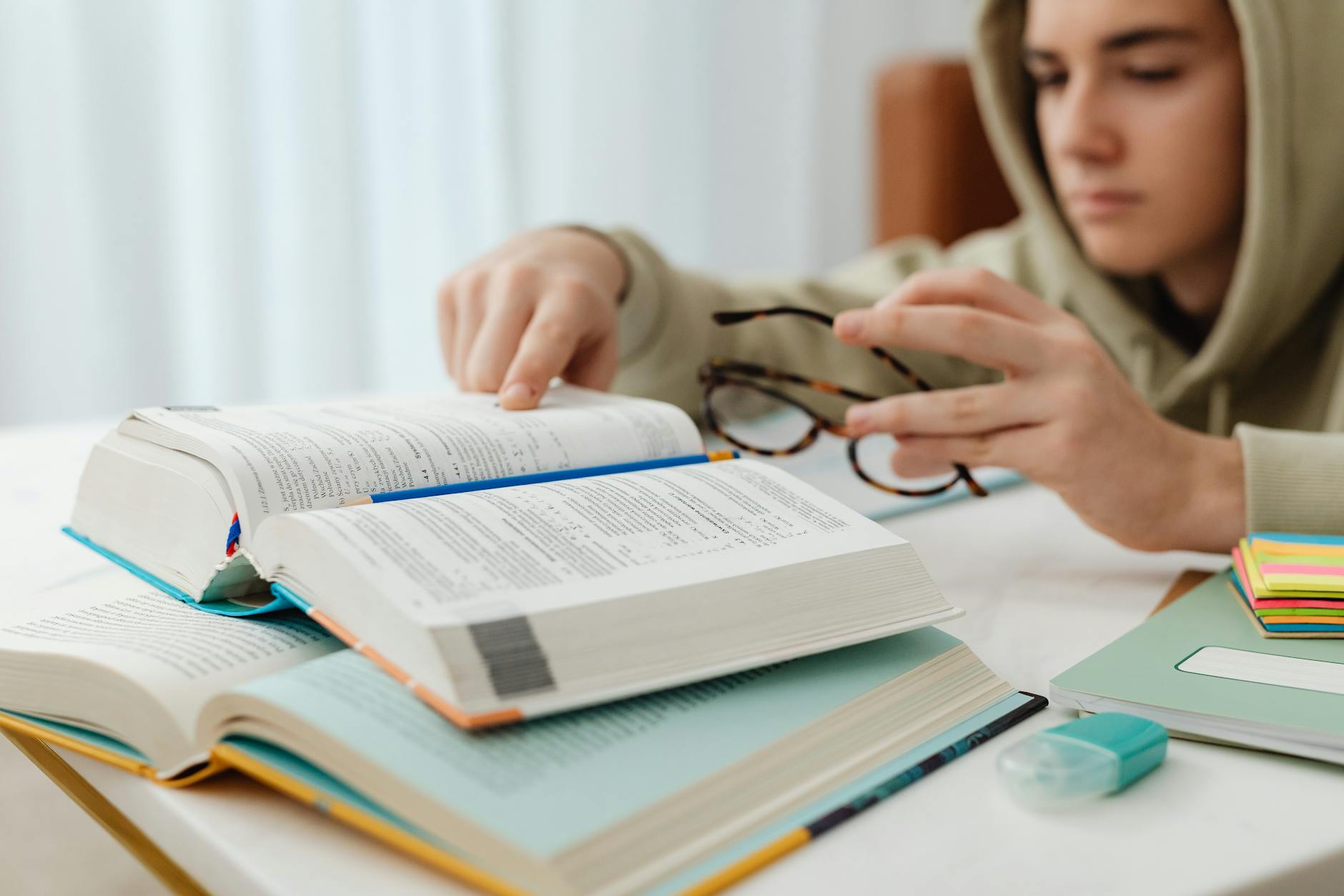 Focused teenager studying with open textbooks, eyeglasses, and notes — UPI Study