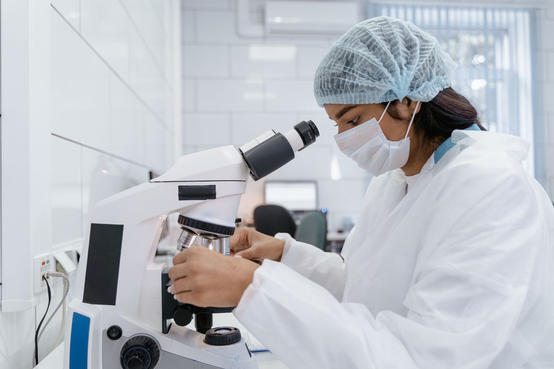 A female scientist wearing protective gear analyzes samples using a microscope in a modern laboratory — UPI Study