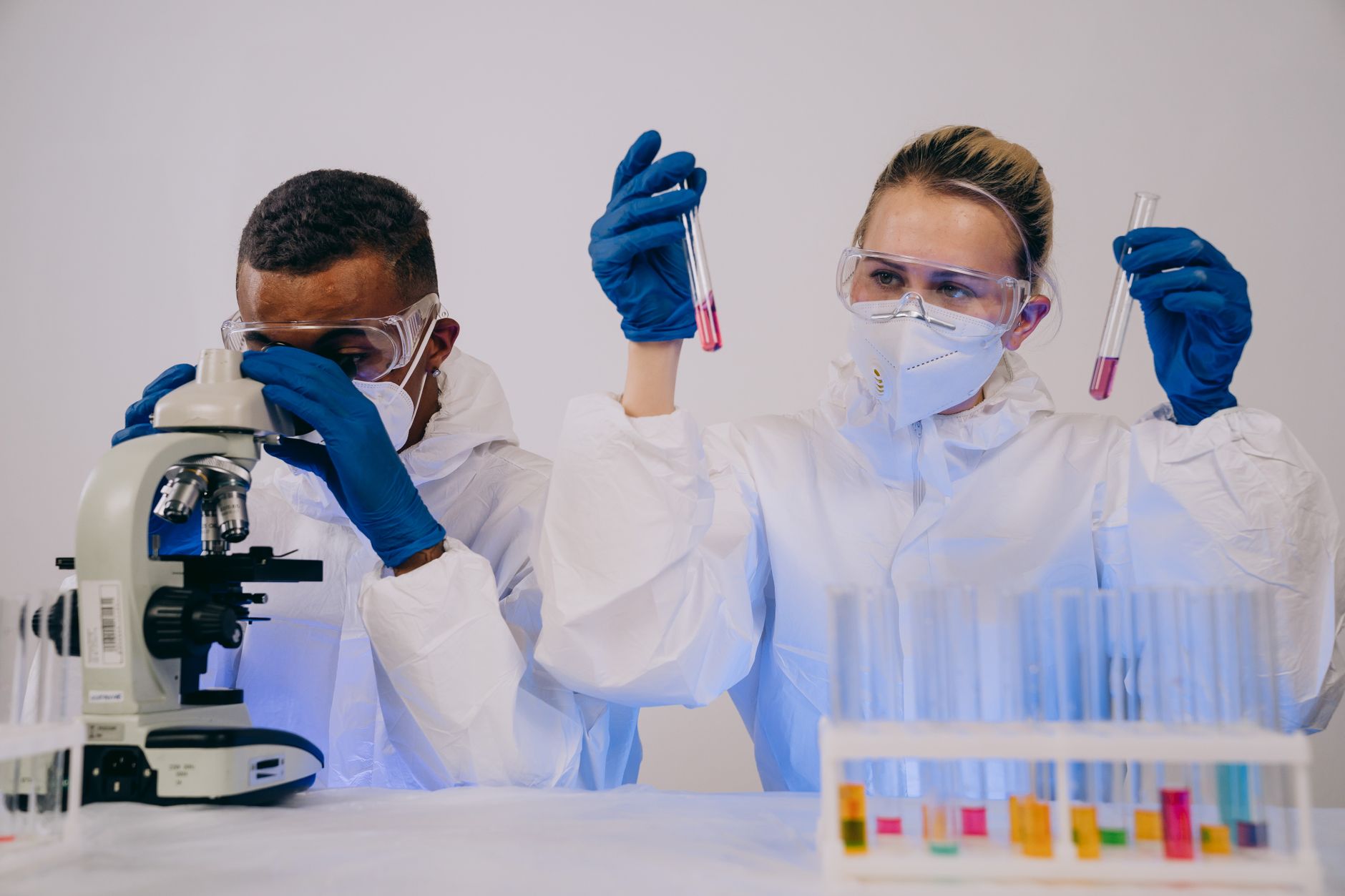 Two scientists in protective gear working with microscope and test tubes in a lab — UPI Study