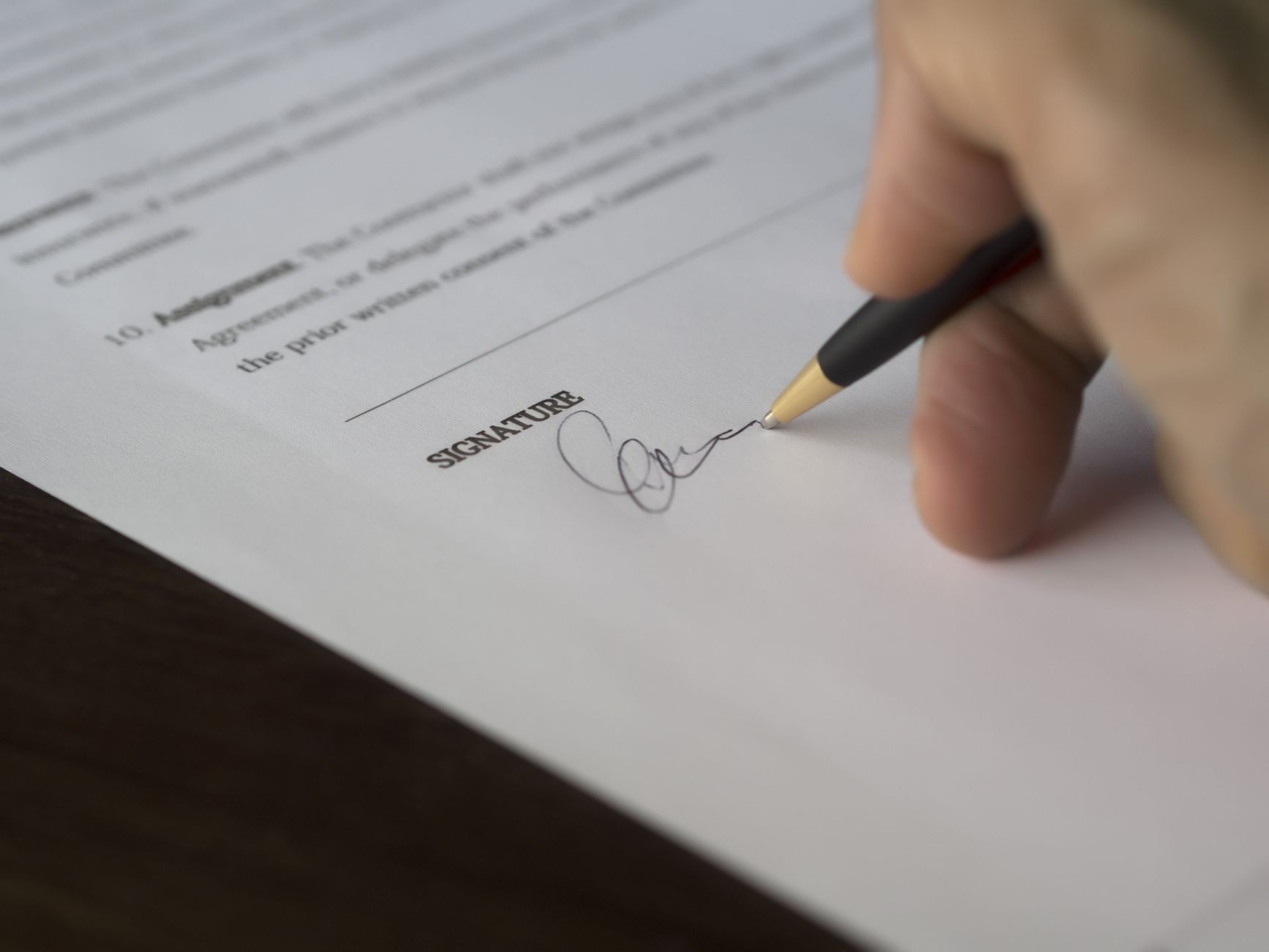 A hand signs a formal contract with a pen on a wooden desk — UPI Study
