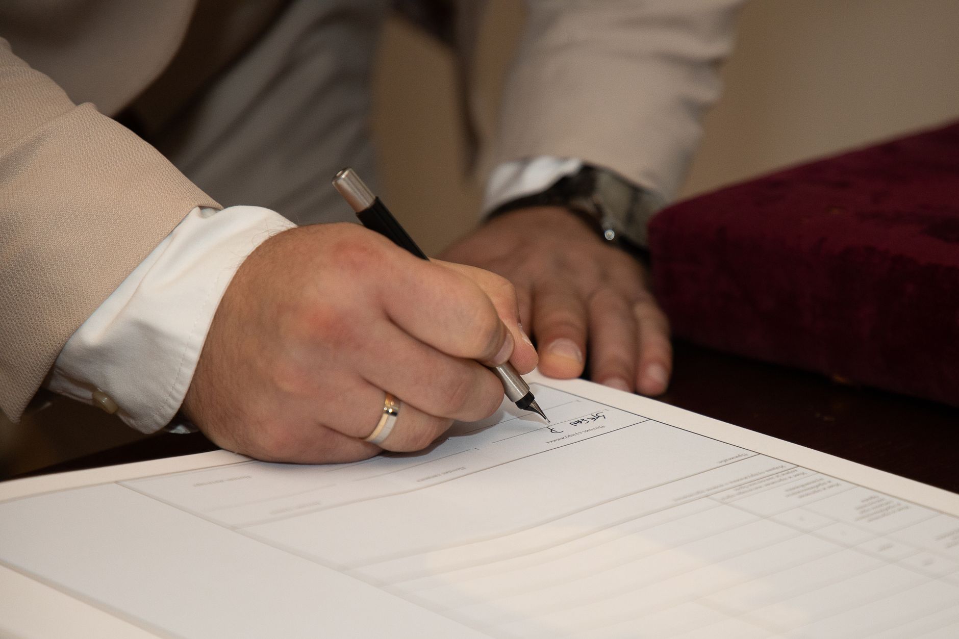 A close-up of a man signing a document, showcasing a wedding ring and pen — UPI Study