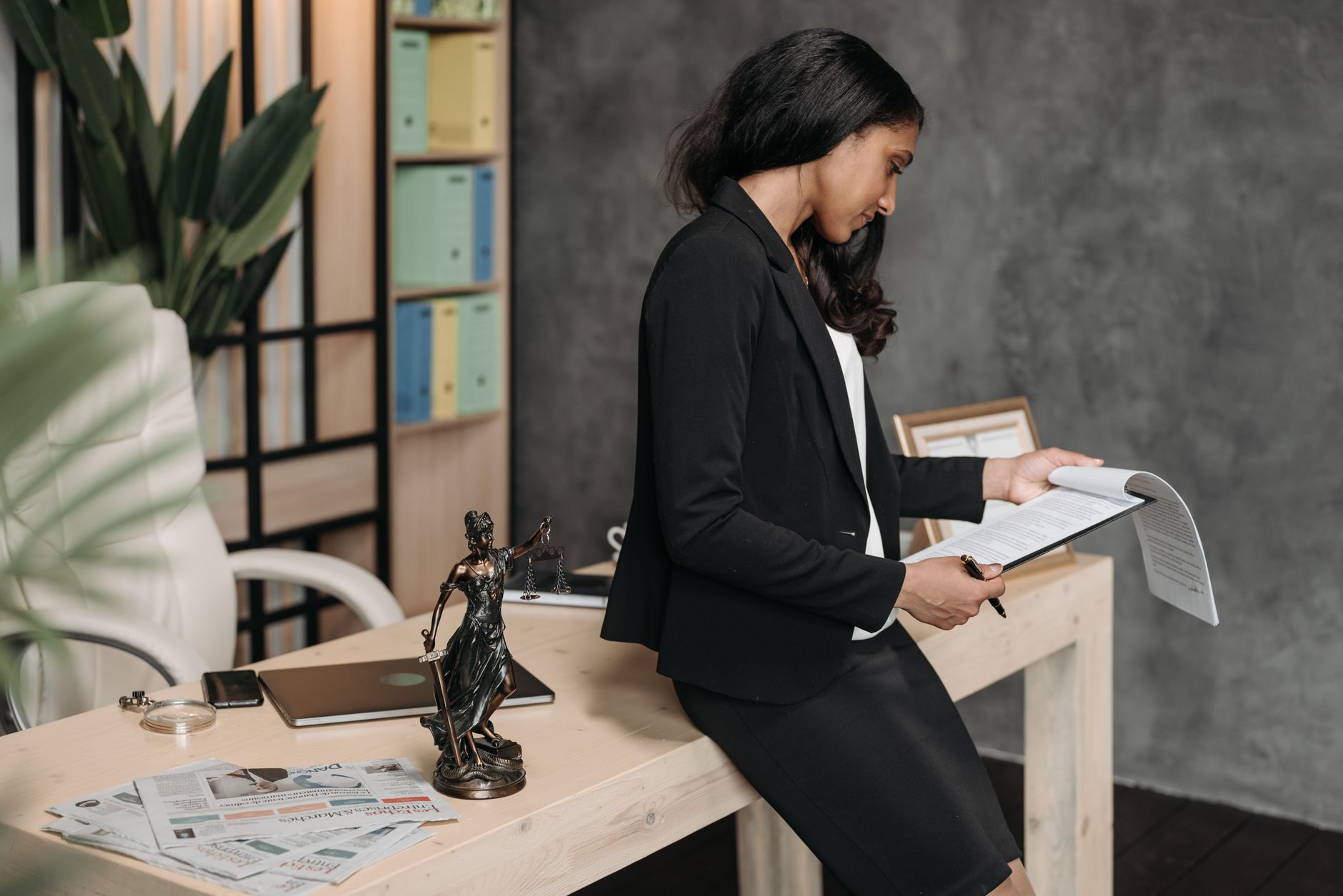 A professional woman in a business suit reviews legal documents at her office desk — UPI Study