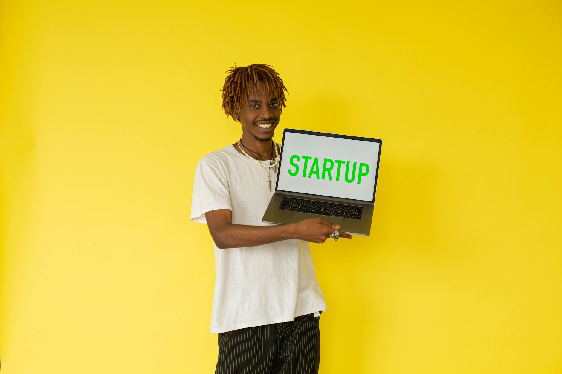 Smiling man holding a laptop with 'STARTUP' on screen against vibrant yellow background — UPI Study