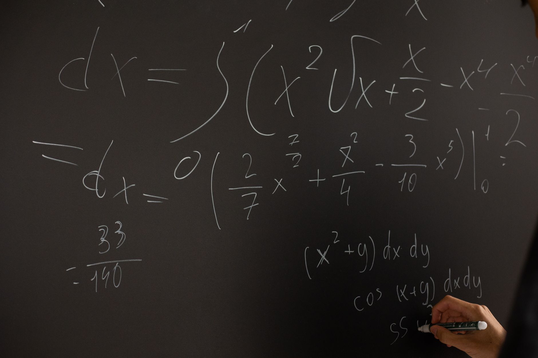 Close-up of hand writing complex math equations on a chalkboard in a classroom setting — UPI Study