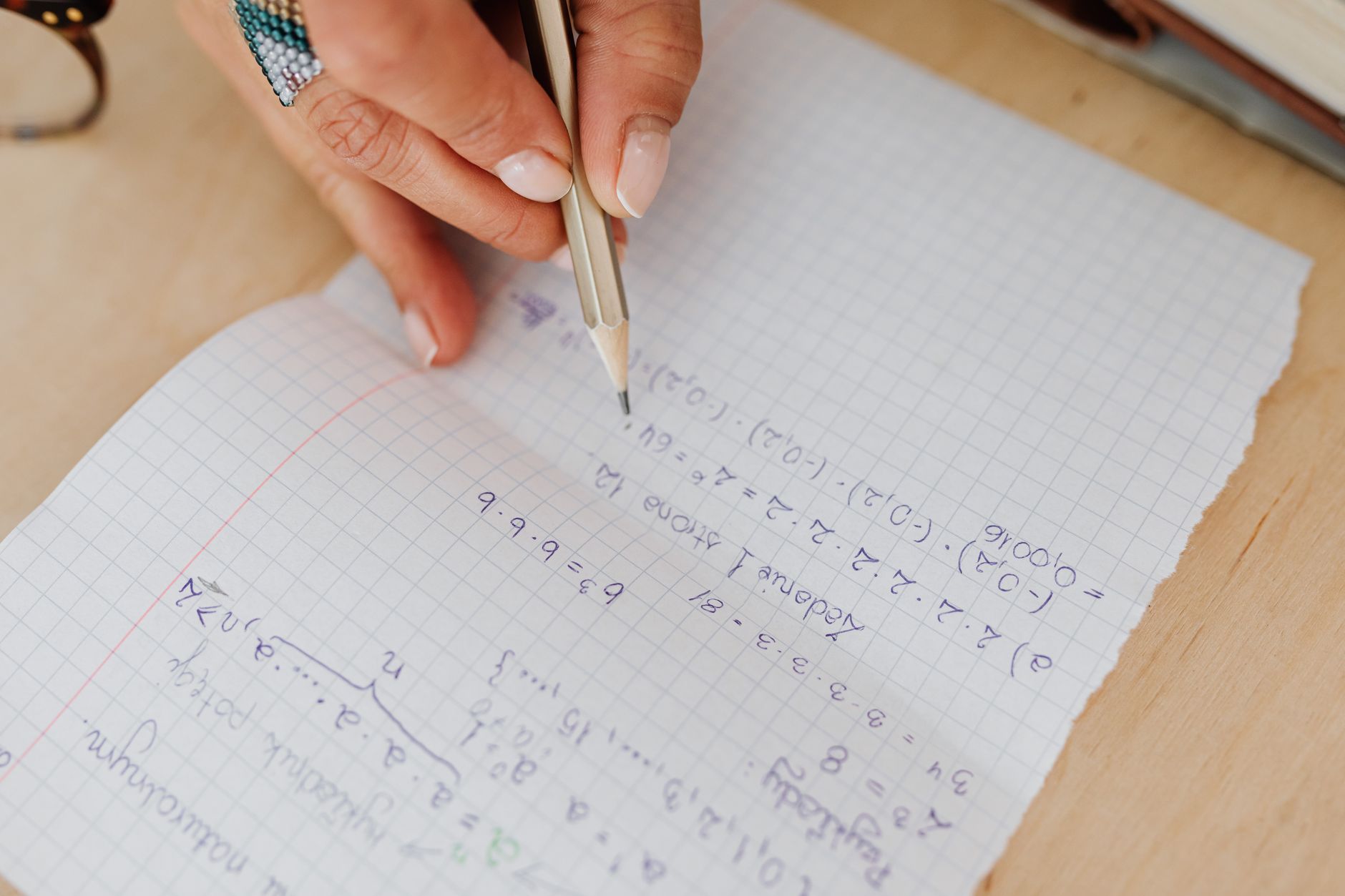 A person writes mathematical equations by hand on grid paper using a pencil, promoting learning — UPI Study