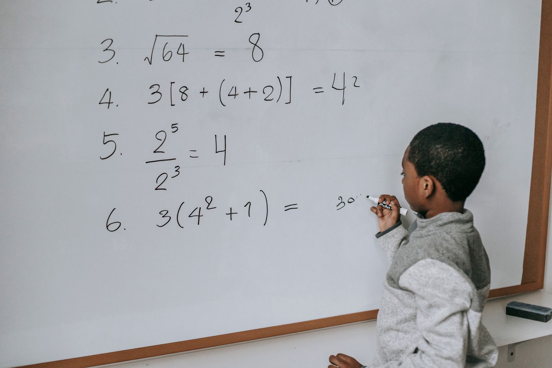 Side view of concentrated African American pupil standing near whiteboard in classroom and solving math examples during lesson at school — UPI Study