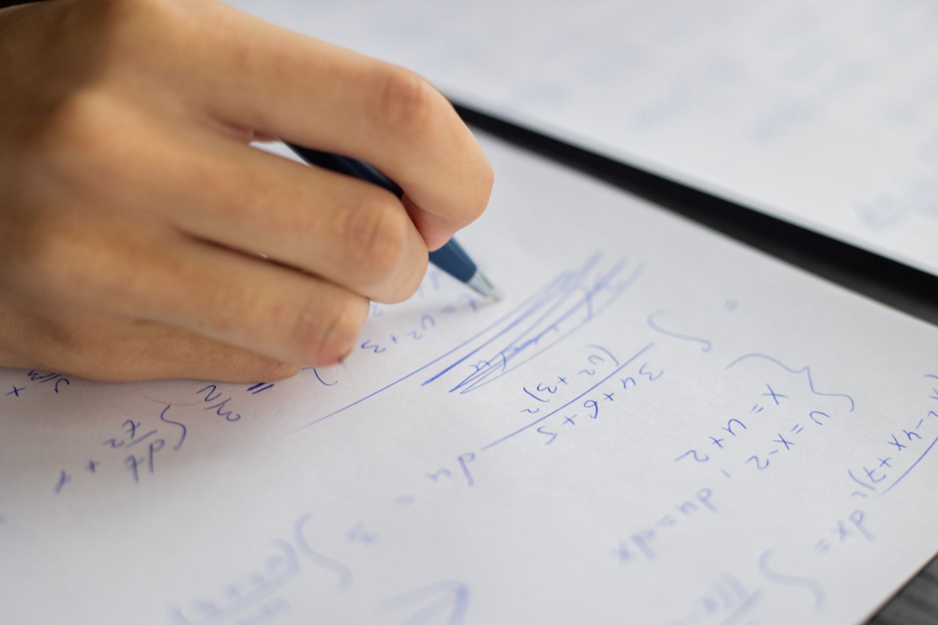 Unrecognizable smart student taking notes on piece of paper while solving mathematical formulas during lesson in classroom on blurred background — UPI Study