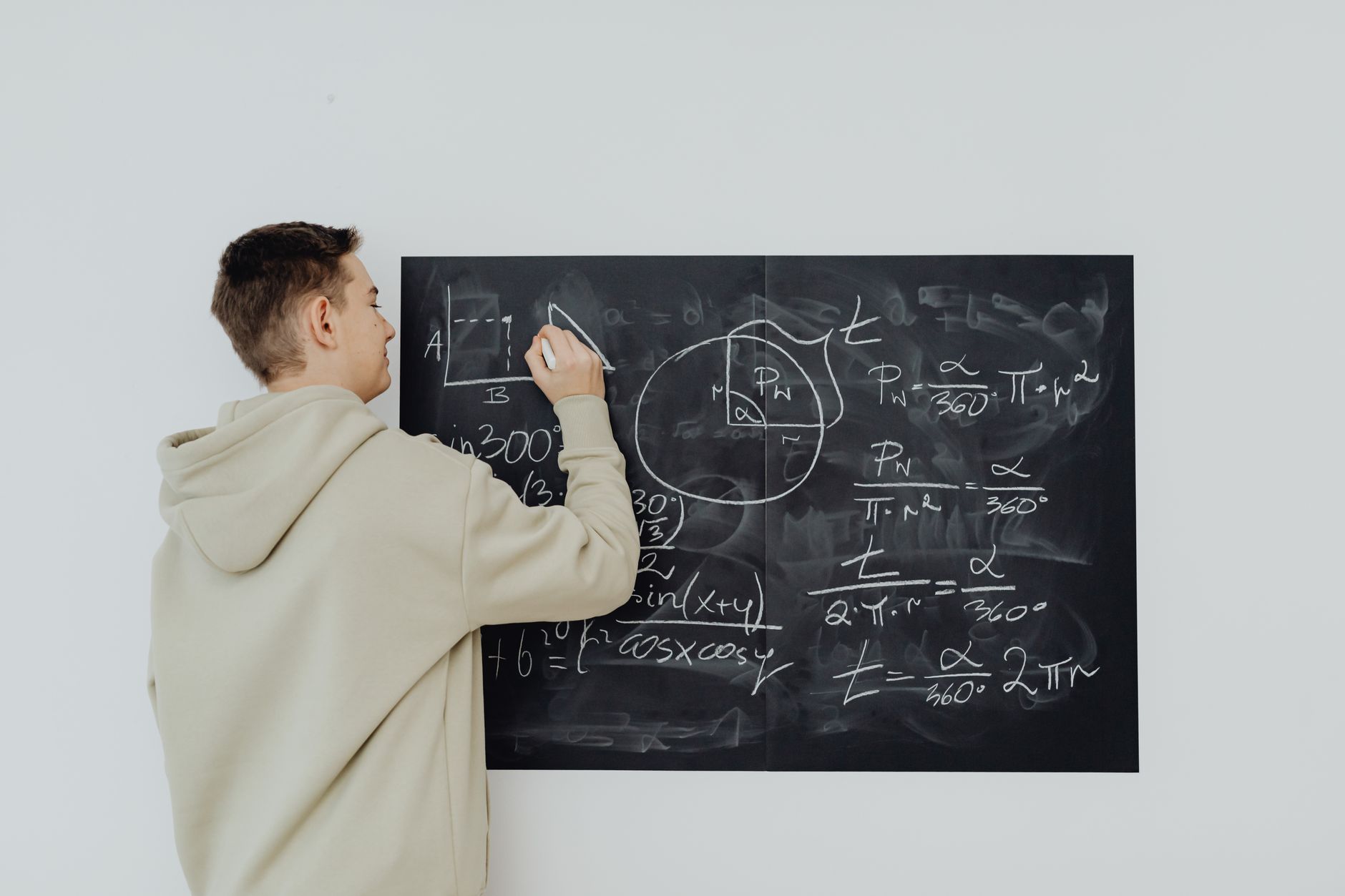 Teen boy in hoodie writes math formulas on a chalkboard, focused on solving algebra equations — UPI Study