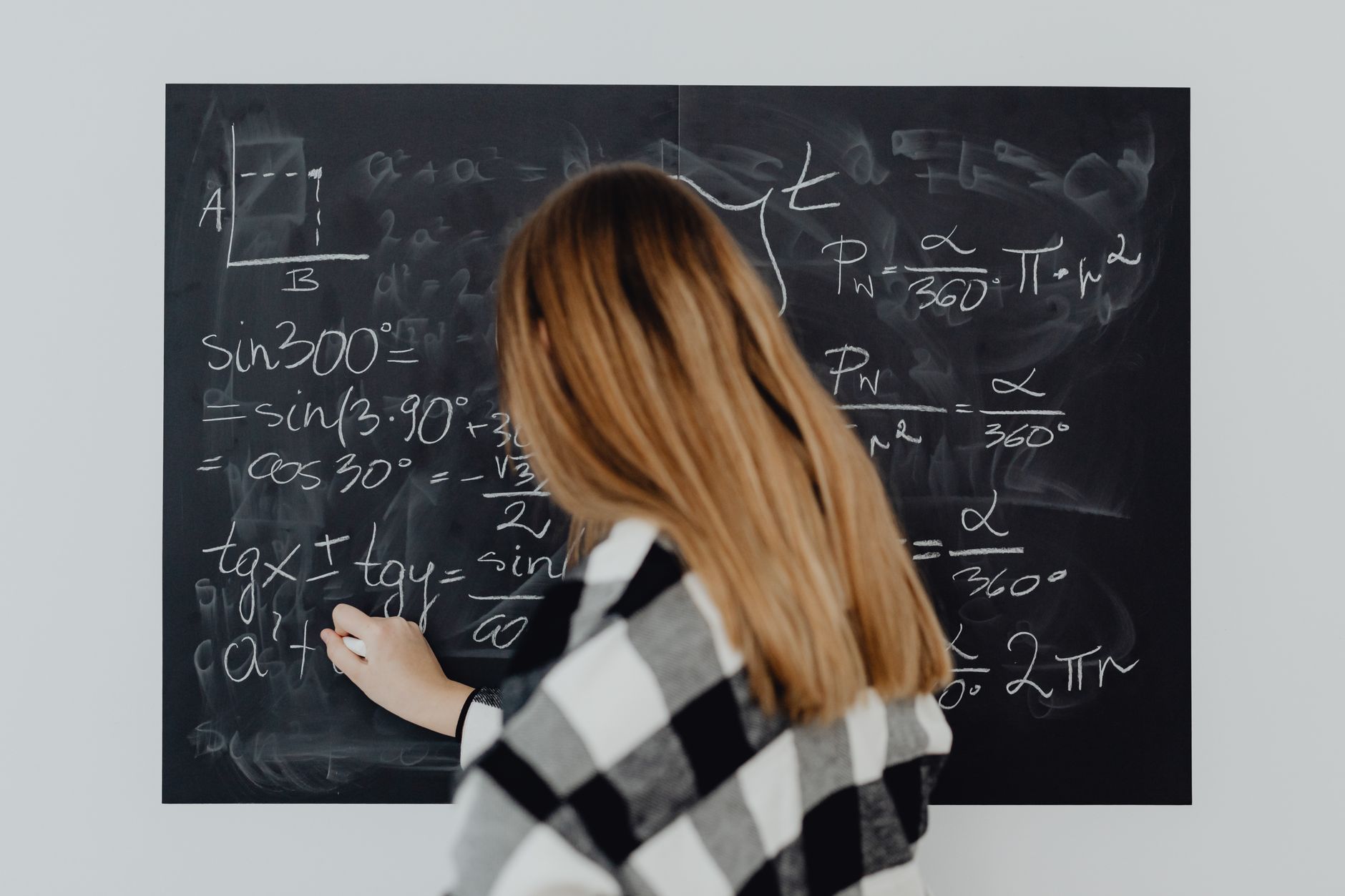 A woman writing mathematical equations on a blackboard, illustrating education and learning — UPI Study