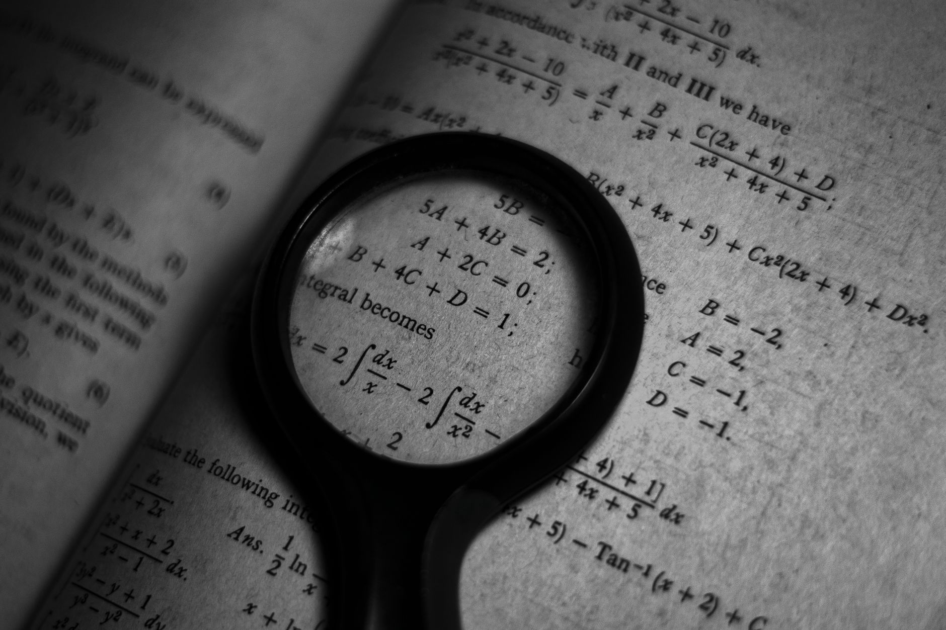A magnifying glass focuses on mathematics formulas in a book, enhancing study and exploration — UPI Study