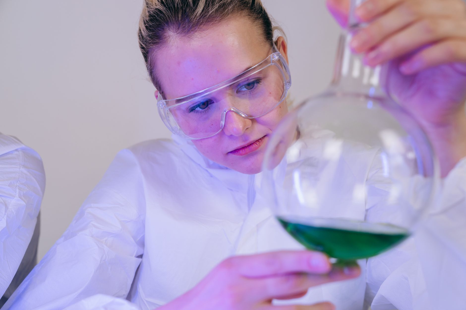 A female scientist closely examines a green solution in a laboratory setting, wearing protective gear — UPI Study