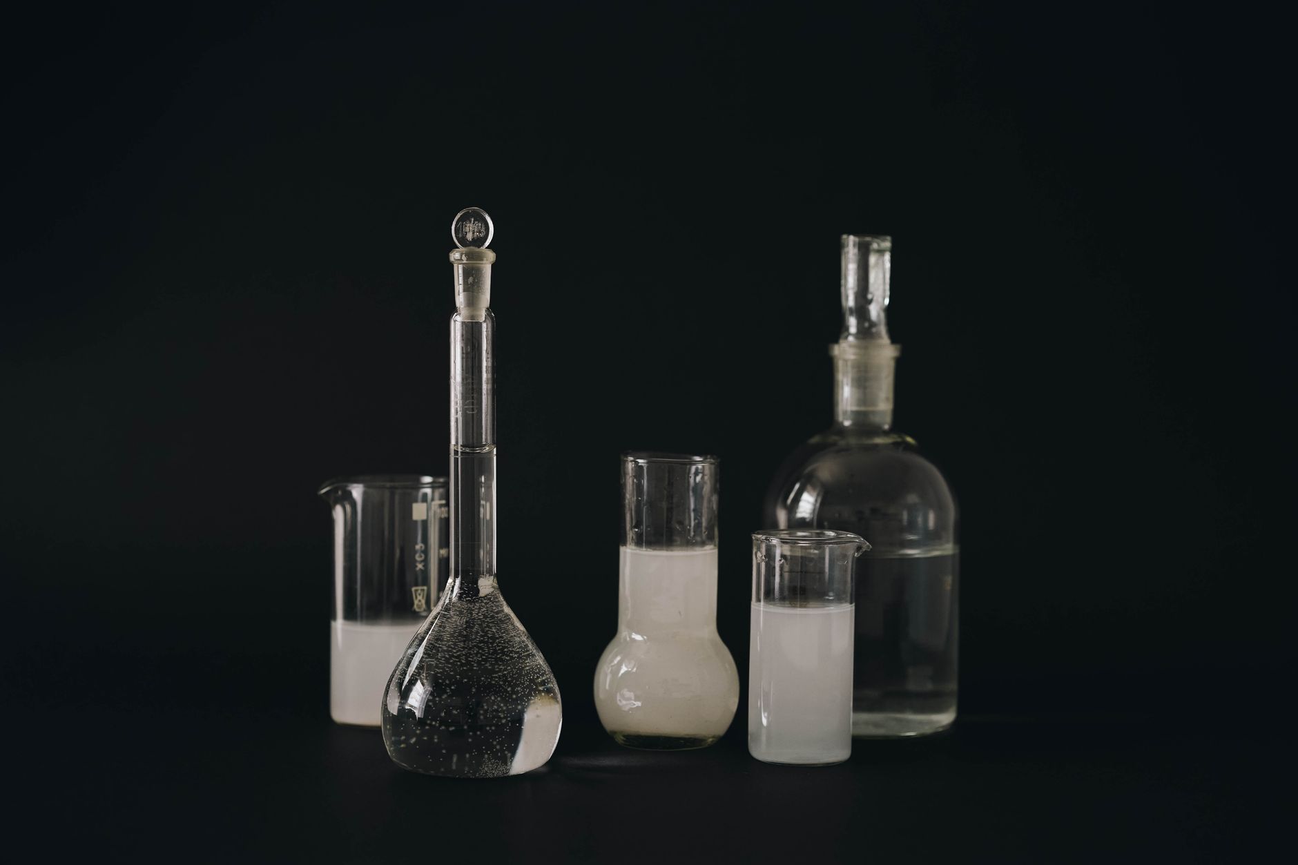 Set of glass laboratory bottles and flasks with liquids on a dark background — UPI Study