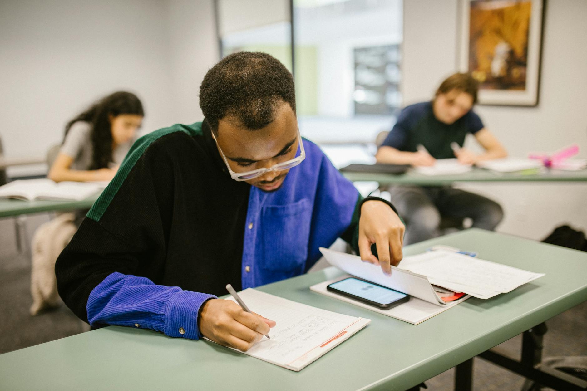 Students taking a test in a classroom setting, focusing on a man writing while others work — UPI Study