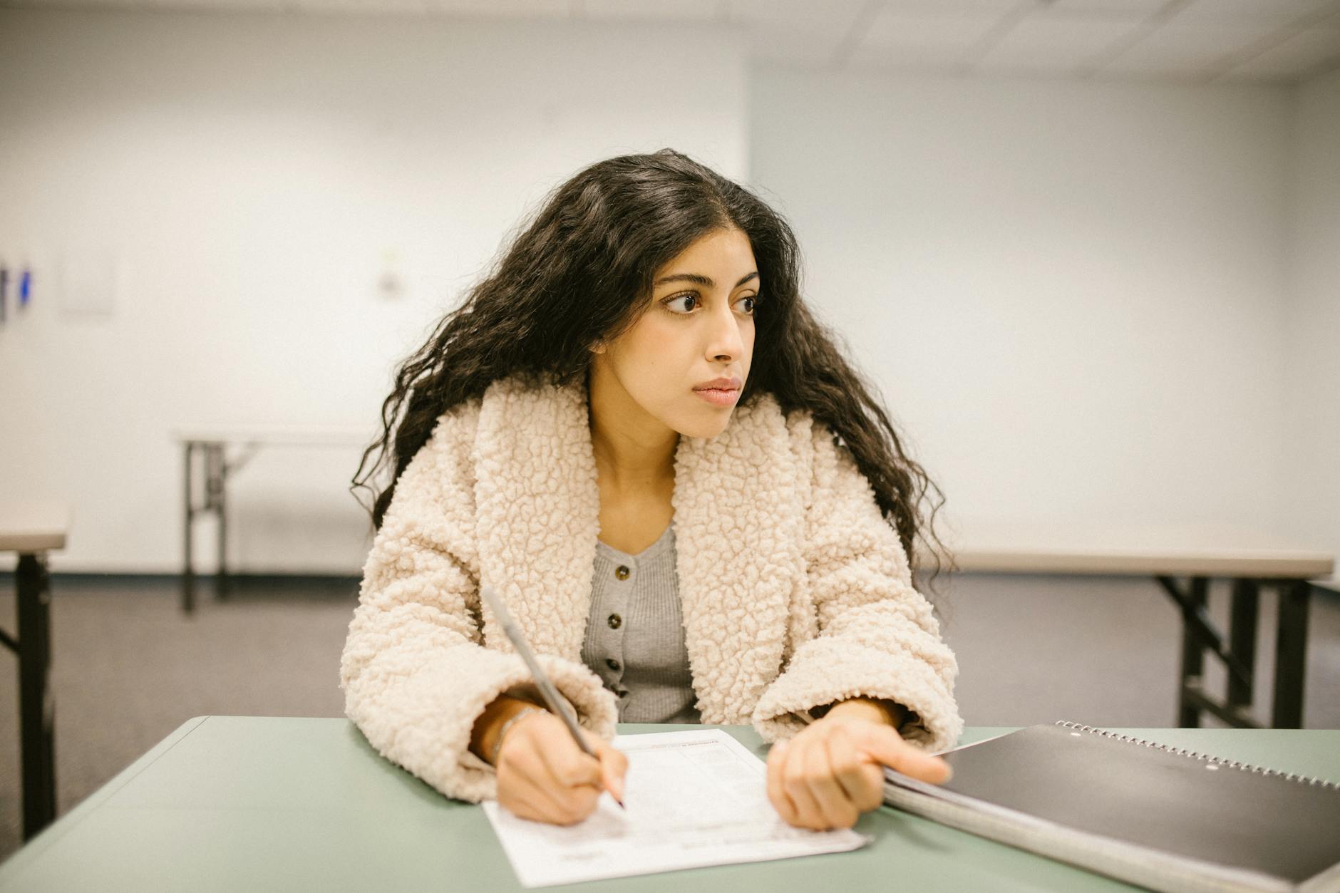 A college student writing on a test paper while looking away in a classroom setting — UPI Study