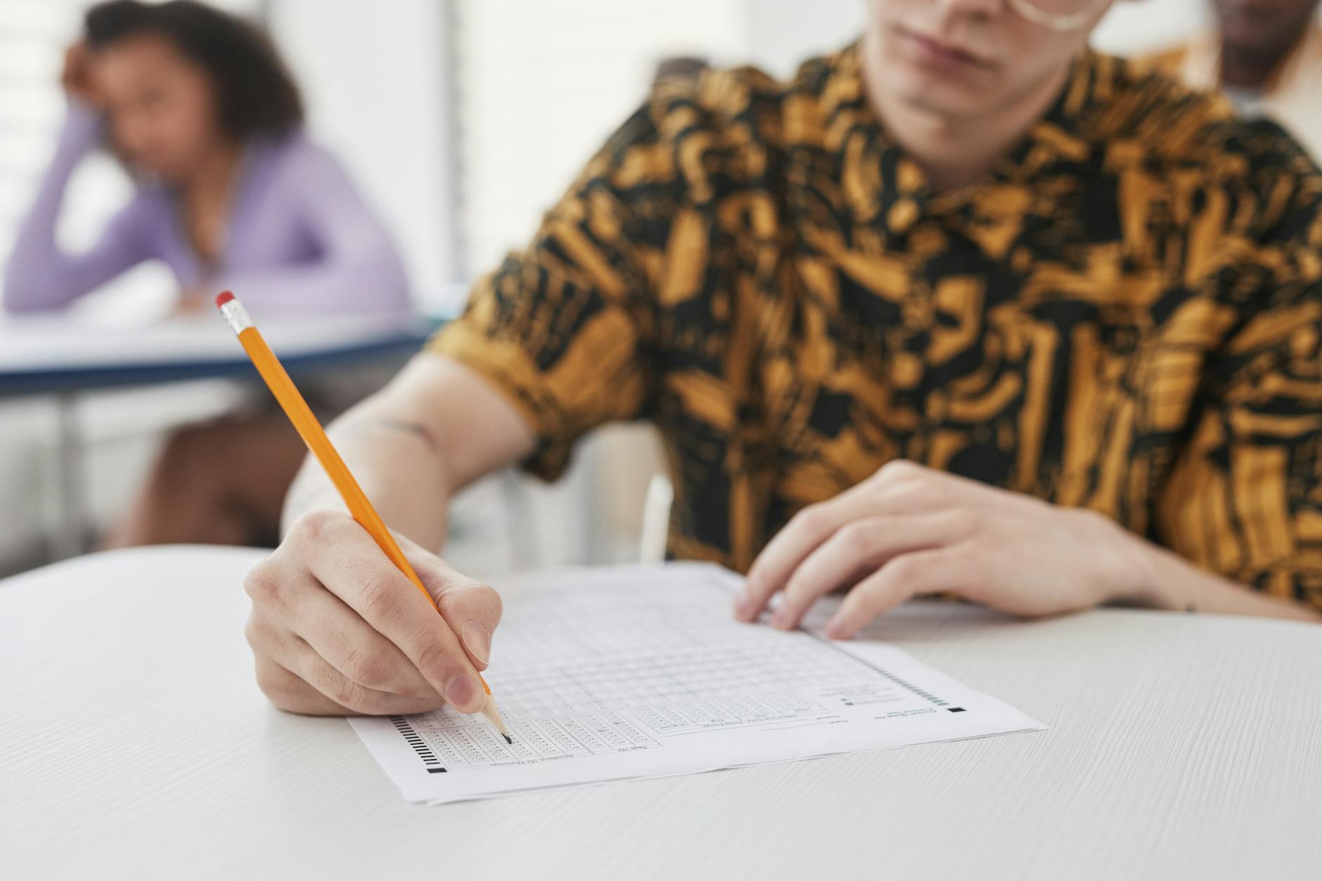 Young adult writing on exam paper in classroom setting, focus on pencil and paper — UPI Study