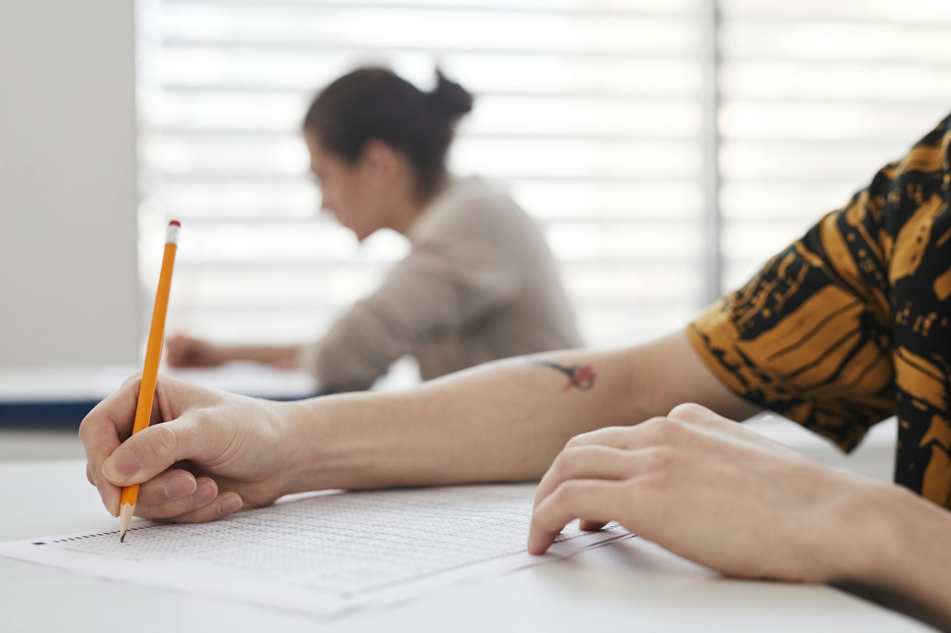 Close-up of student's hands writing on exam sheet, indoors with blurred background — UPI Study