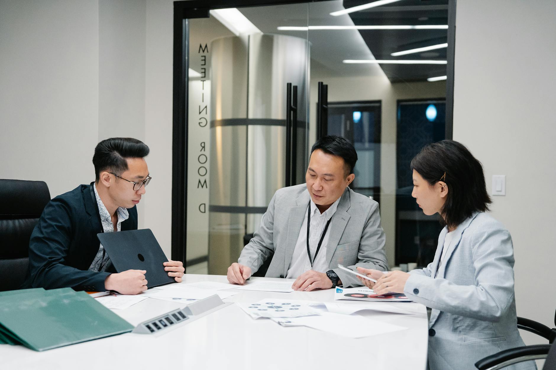 Business meeting with three professionals collaborating in a modern conference room setting — UPI Study
