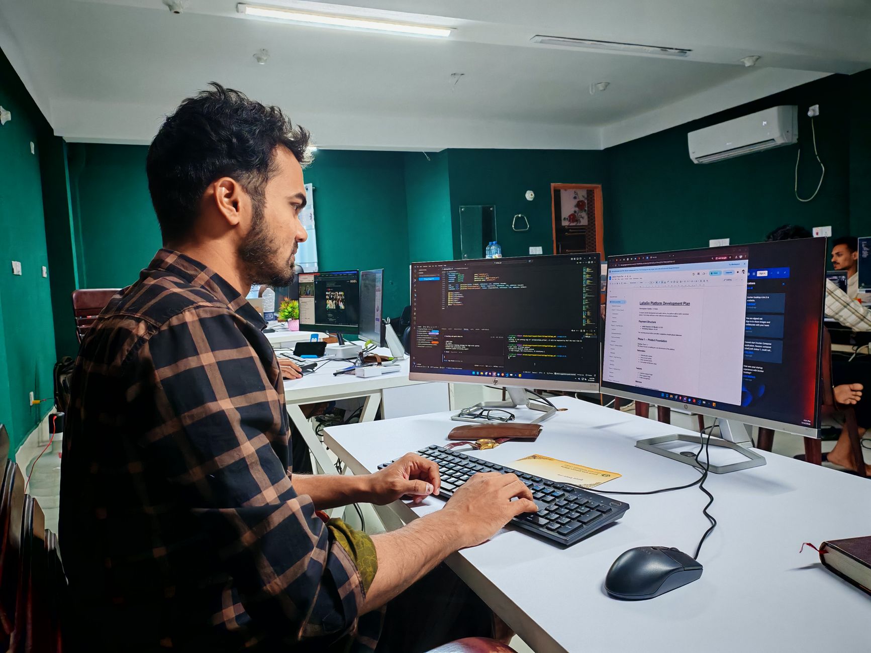 A software developer working on code at a dual monitor setup in a modern office — UPI Study