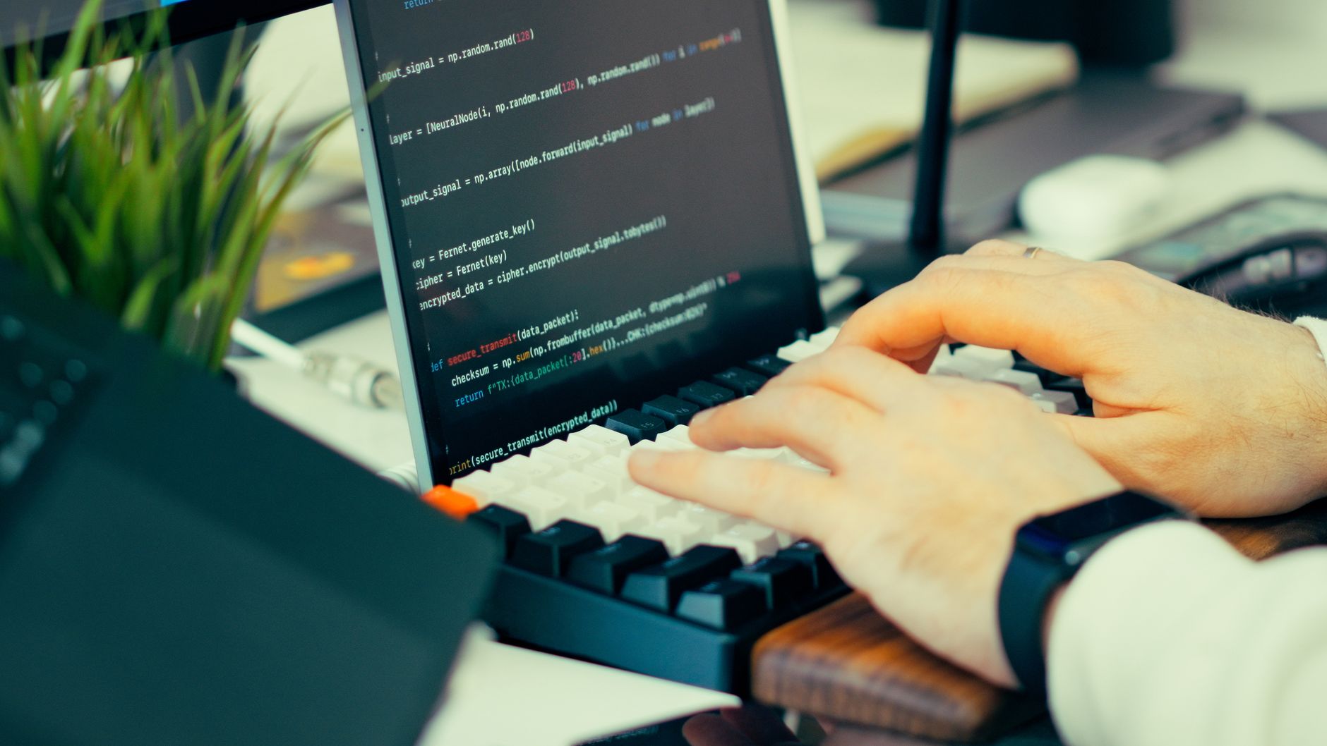 Close-up view of a developer typing code on a keyboard with a computer screen showing scripts — UPI Study