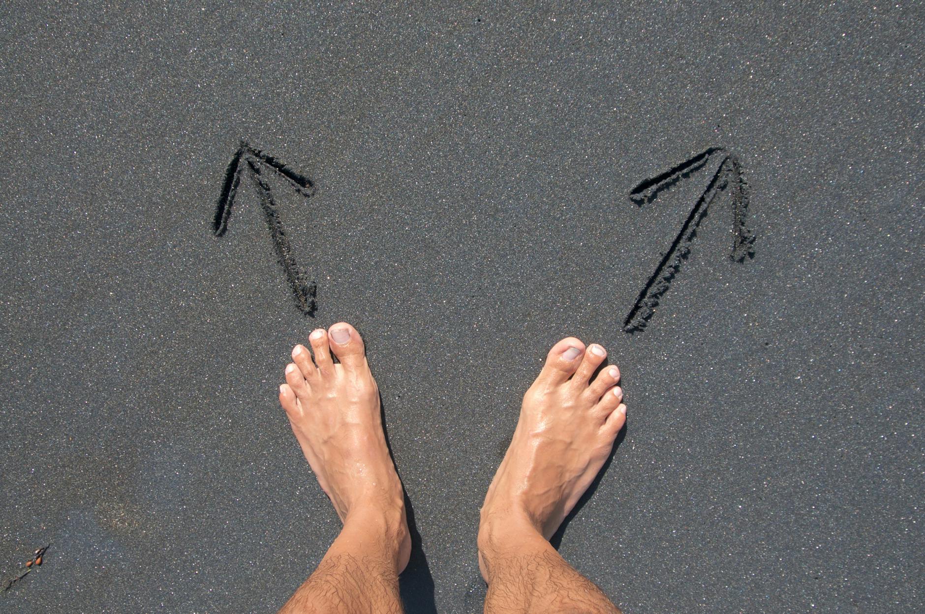 A pair of bare feet on Bali's beach sand with arrows drawn, symbolizing choice and direction — UPI Study