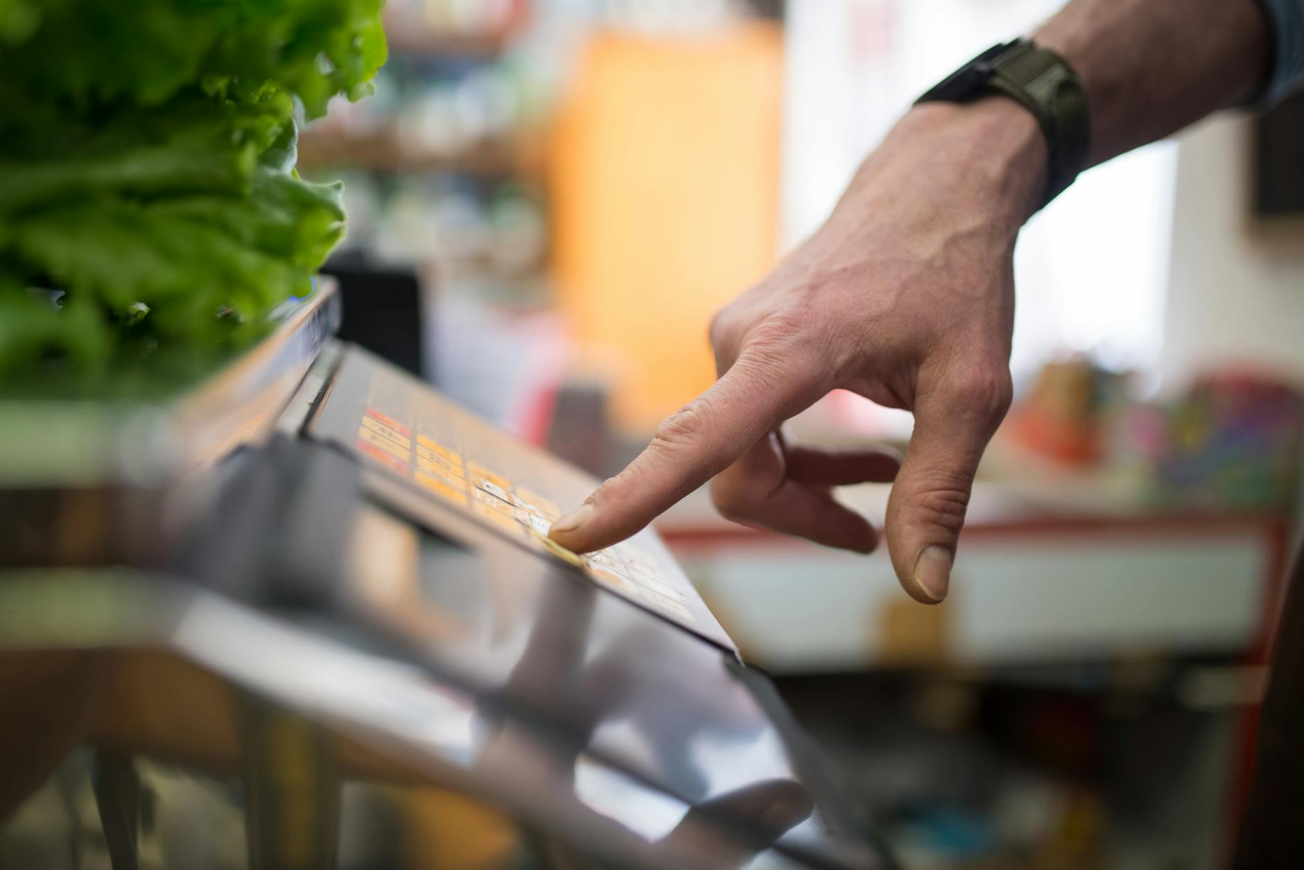 A hand interacting with a digital weighing scale in a produce section, emphasizing technology in shopping — UPI Study