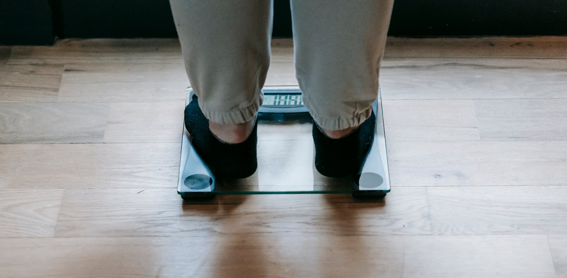 Back view of crop faceless obese female in socks weighing on glass scale placed on wooden floor in light room in daytime — UPI Study
