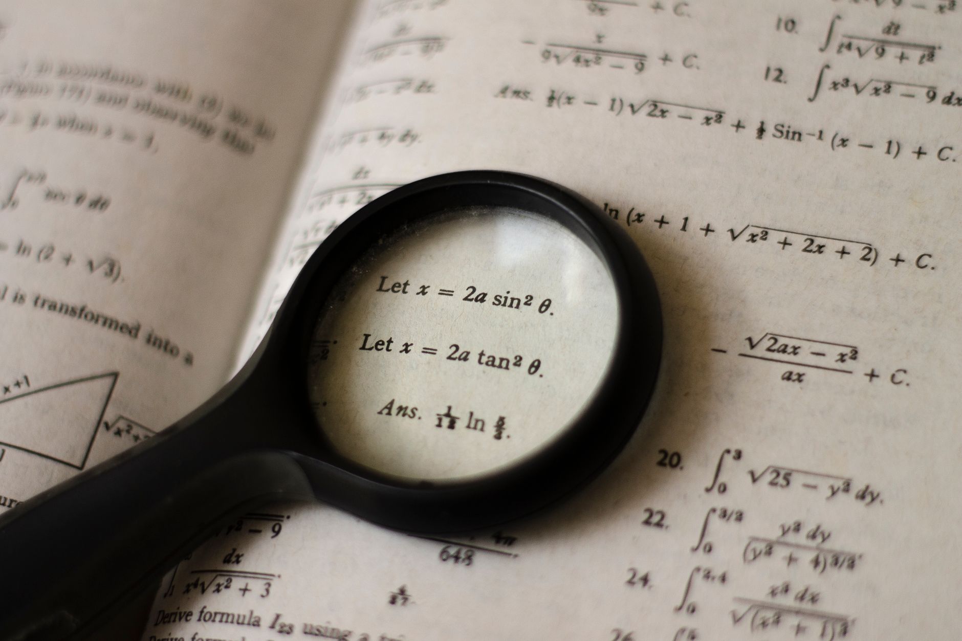 A magnifying glass focusing on mathematical equations in a textbook, symbolizing detailed study — UPI Study