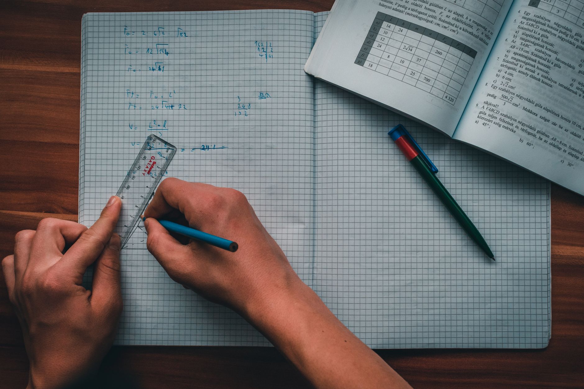 A person writes mathematical equations in a notebook using a ruler and pencil, focused on solving problems — UPI Study
