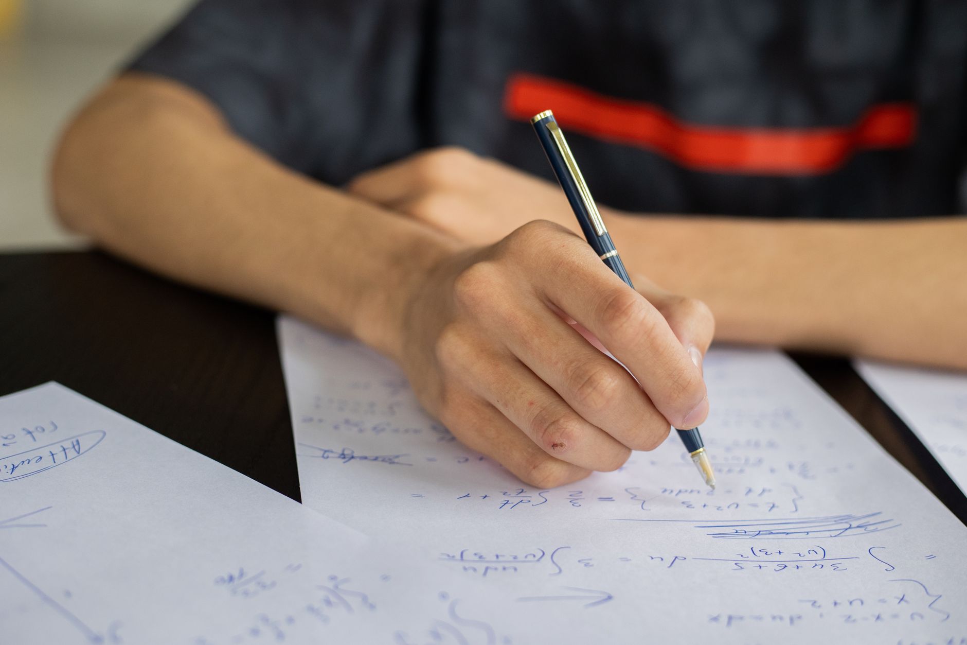 Unrecognizable smart male student with pen  taking notes while solving equations at table during lesson in classroom on blurred background — UPI Study