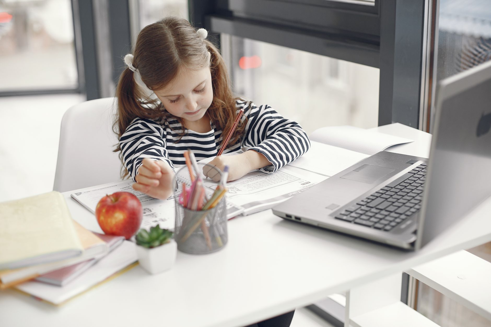 A young girl studies at home using a laptop, engaged with her homework and school supplies — UPI Study