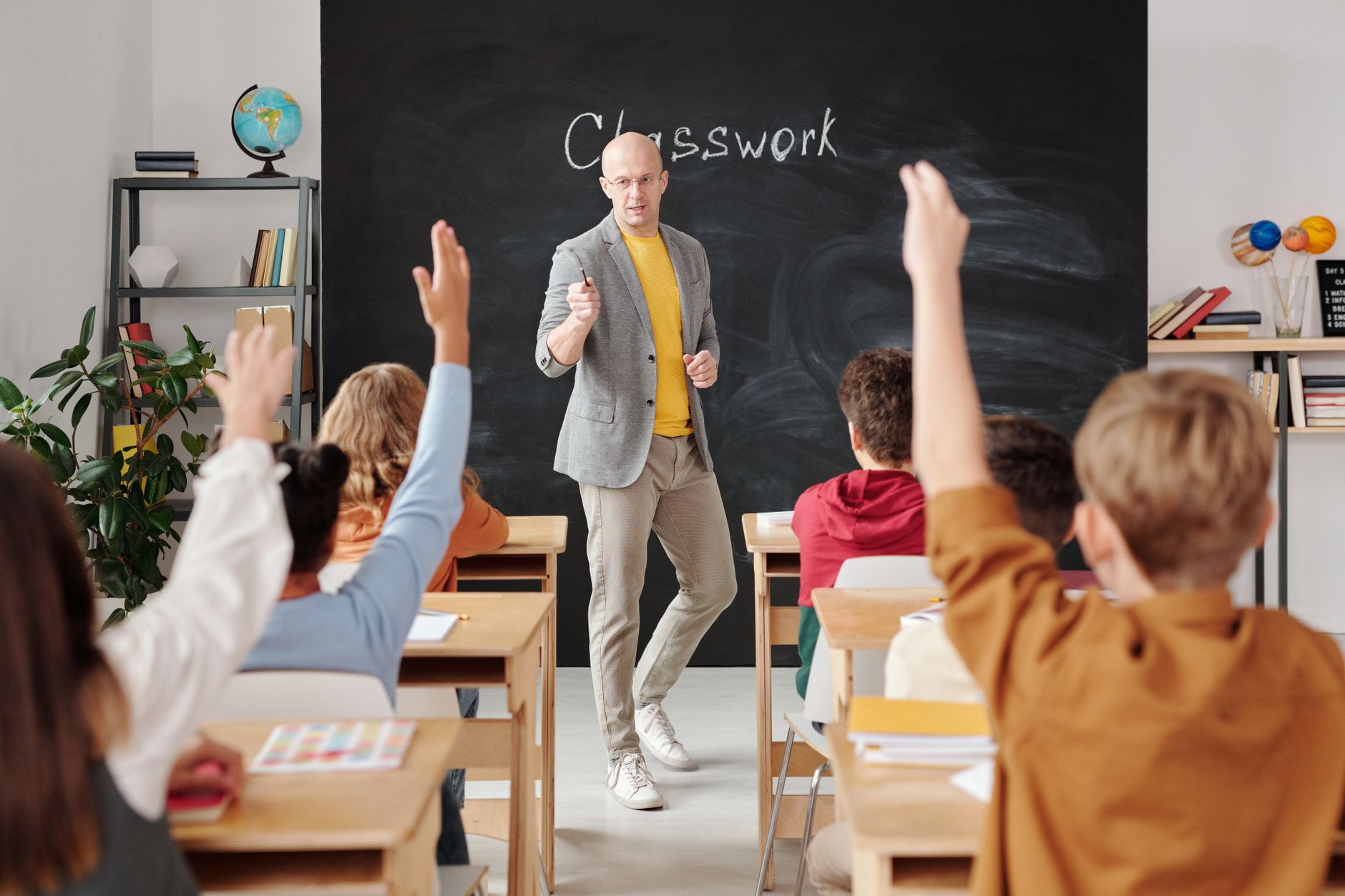Teacher interacting with students raising hands in a classroom setting — UPI Study
