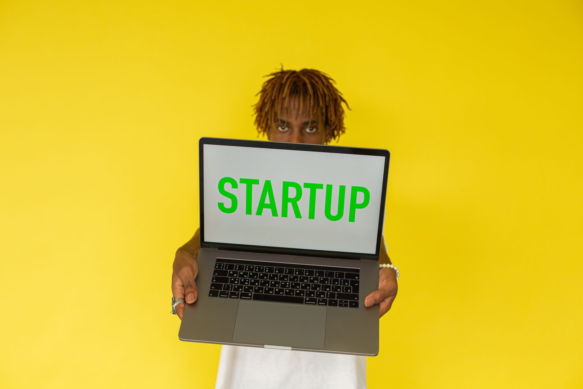 A young black man holds a laptop displaying 'Startup' against a vibrant yellow background — UPI Study