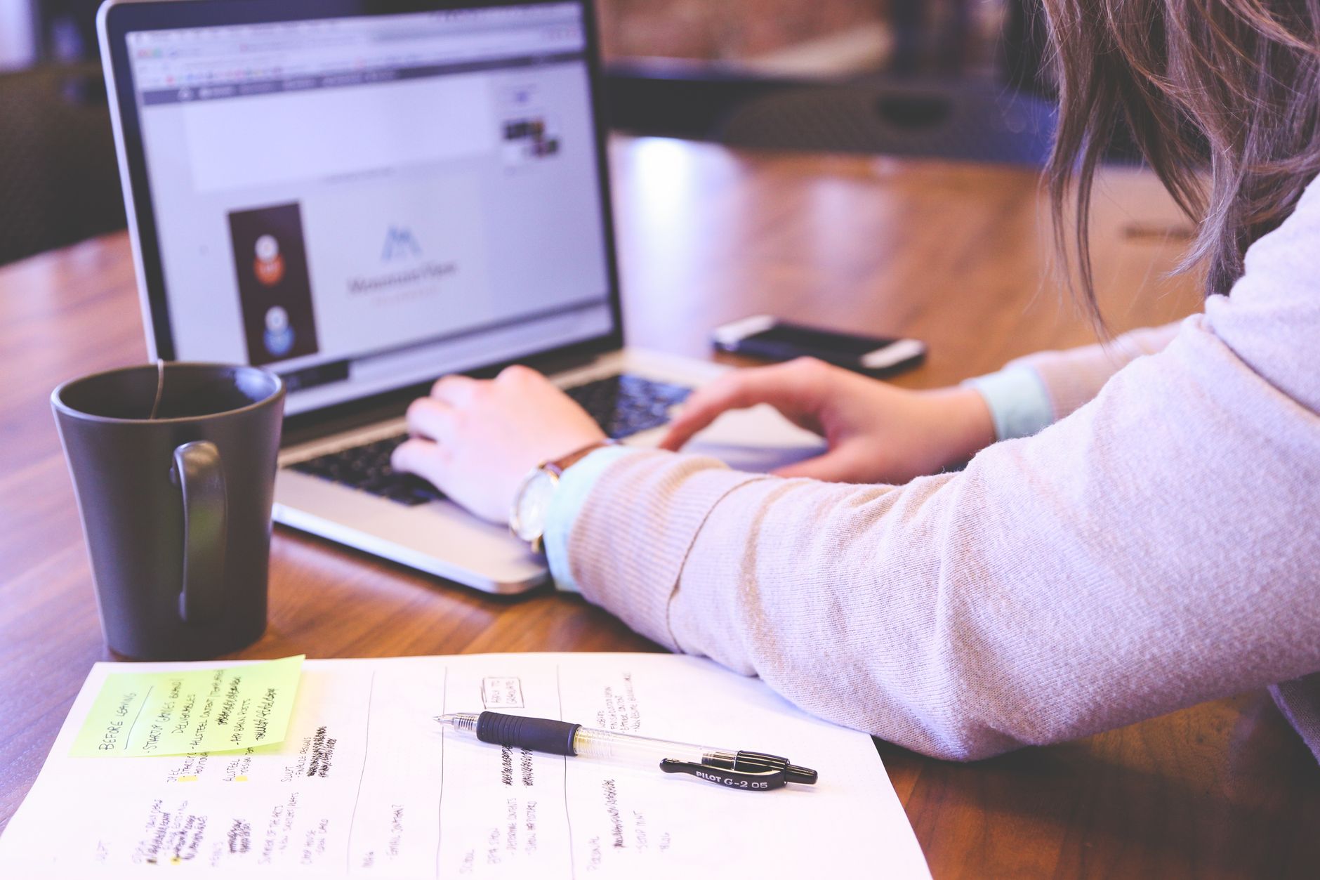 Businesswoman typing on laptop with notes and coffee on wooden desk — UPI Study