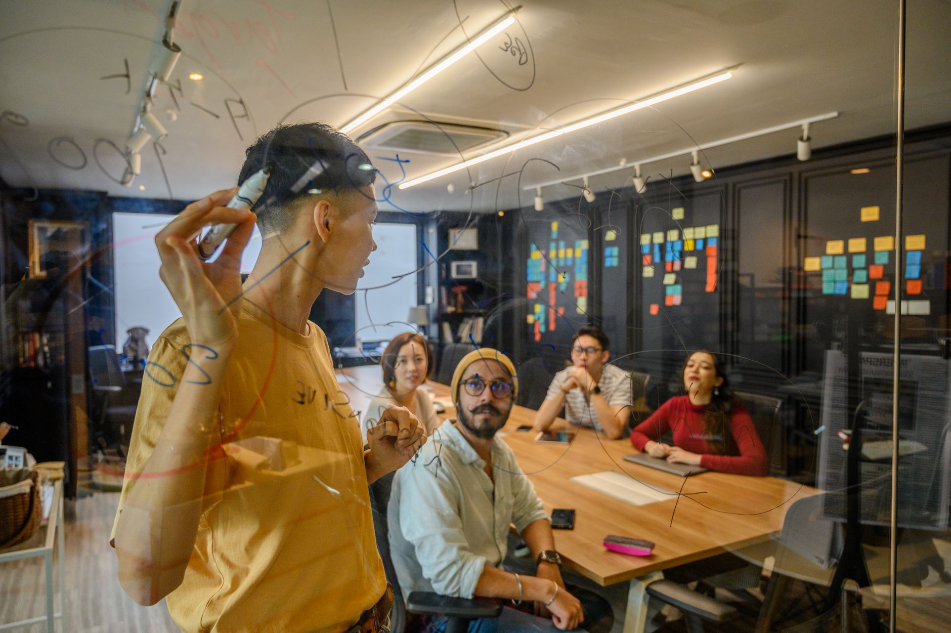 Group of professionals collaborating in an office, brainstorming on glass board — UPI Study