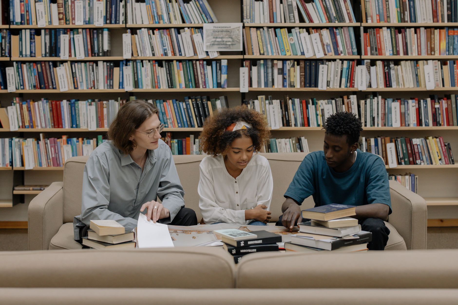 Three students engaged in group study session surrounded by bookshelves — UPI Study