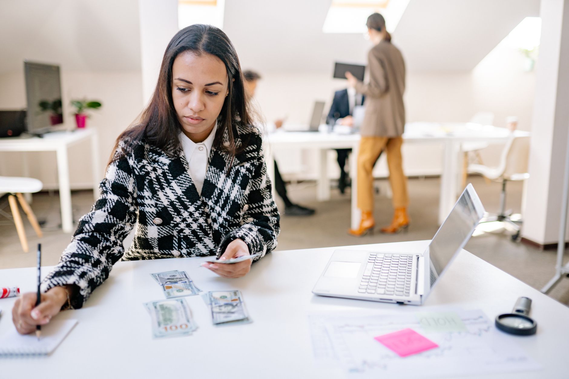 Businesswoman calculating finances with cash and a laptop in a modern office — UPI Study