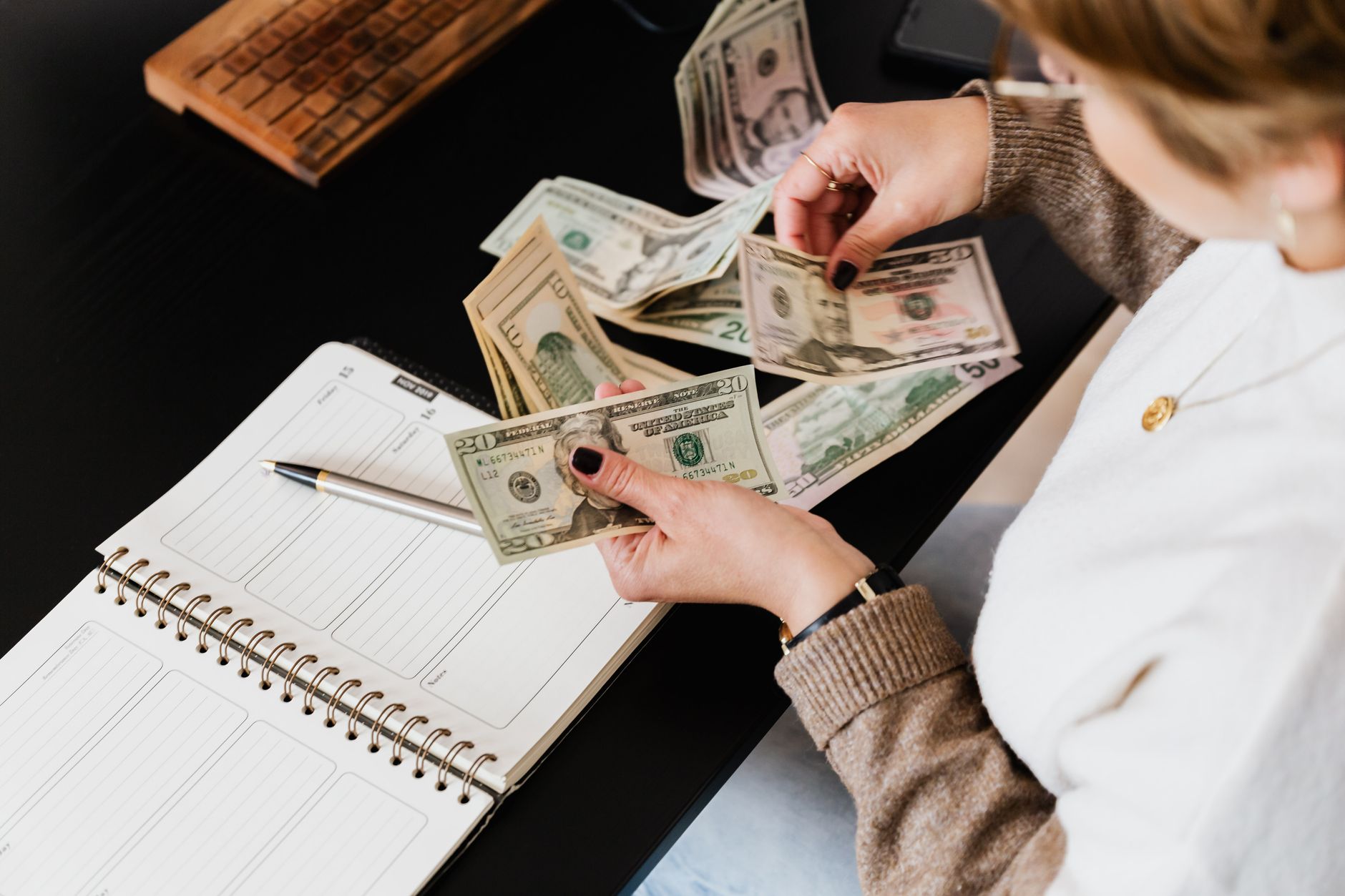 Woman organizing finances, counting dollar bills at desk with open notebook — UPI Study