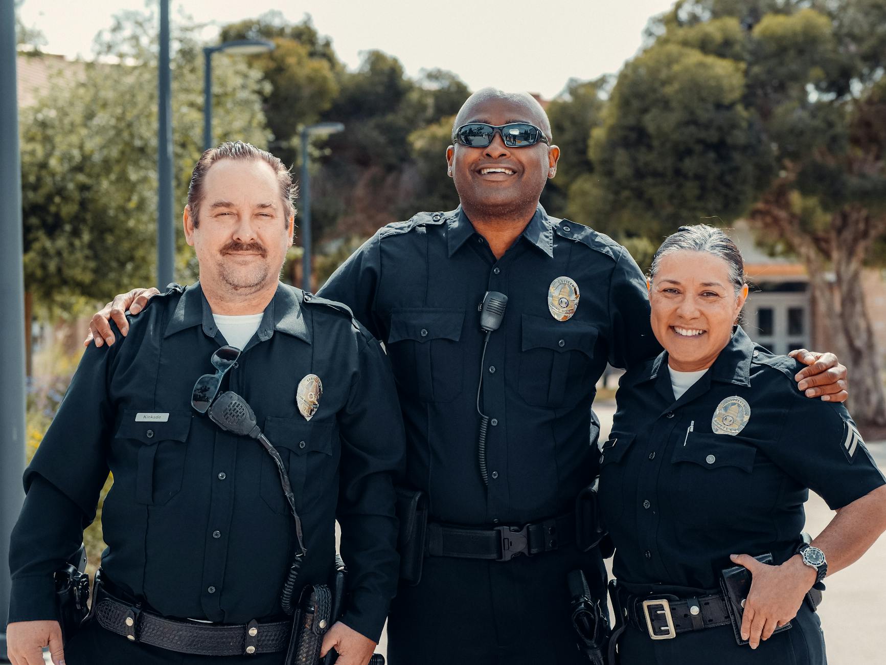 Three police officers in uniform smiling together outdoors, symbolizing community and law enforcement — UPI Study