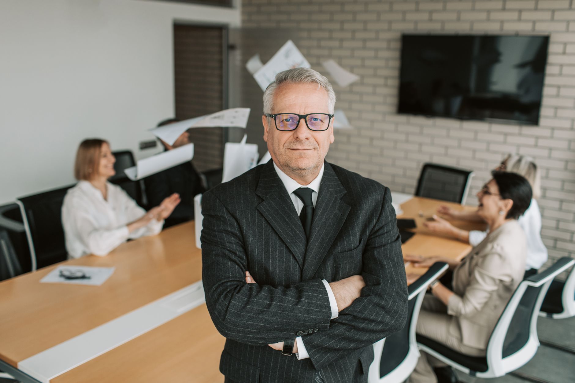 Business executive standing confidently in meeting room with team engaged in discussion behind — UPI Study