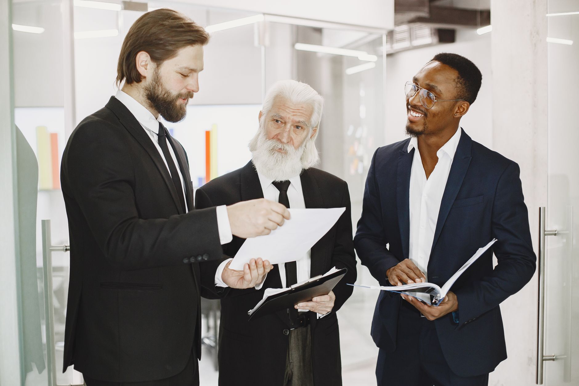Three businessmen in suits discussing documents in a modern office setting, engaging in teamwork — UPI Study